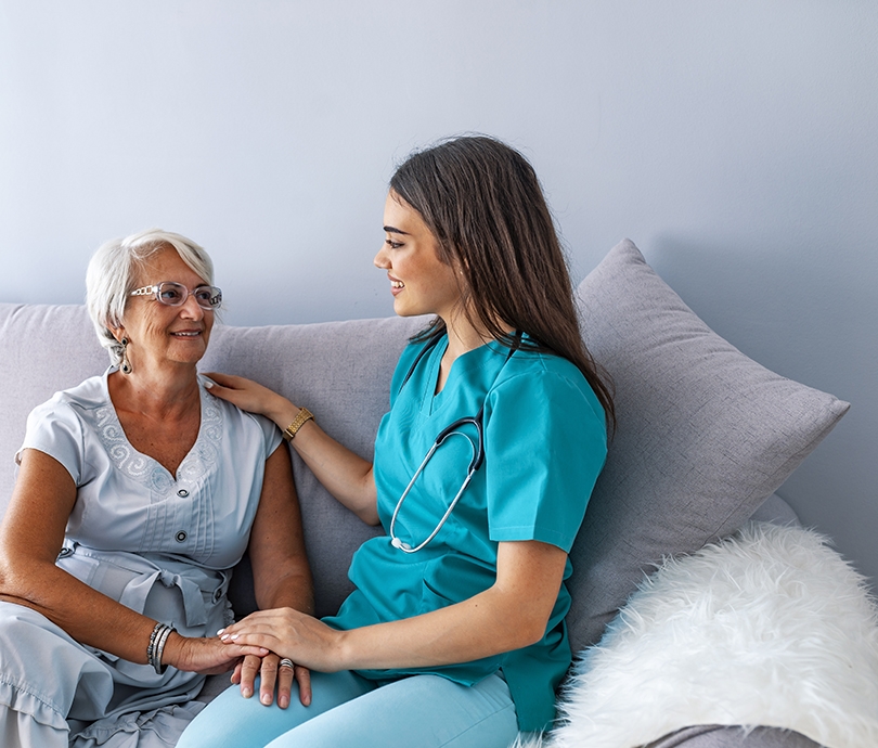 Friendly relationship between smiling caregiver in uniform and happy elderly woman. Supportive young nurse looking at elder woman. Young caring lovely caregiver and happy ward